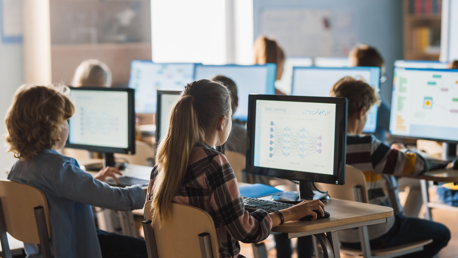 Children in a classroom using desktop devices to learn