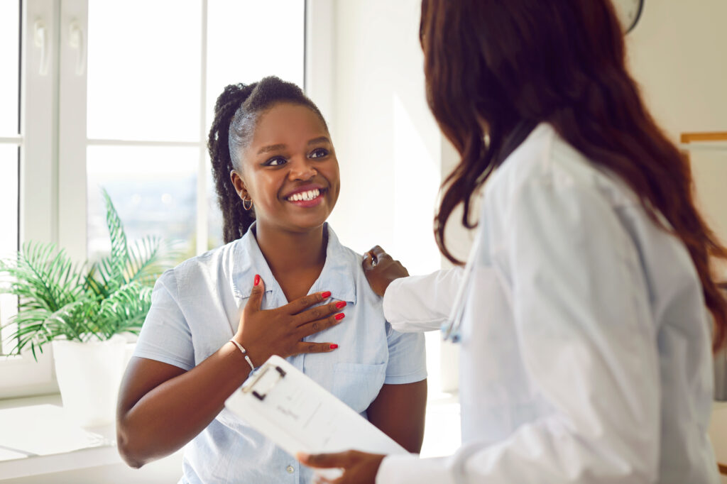 Black woman doctor or nurse is talking with a happy patient in a hospital. The atmosphere is one of genuine care, with the medical professional engaging in a conversation.